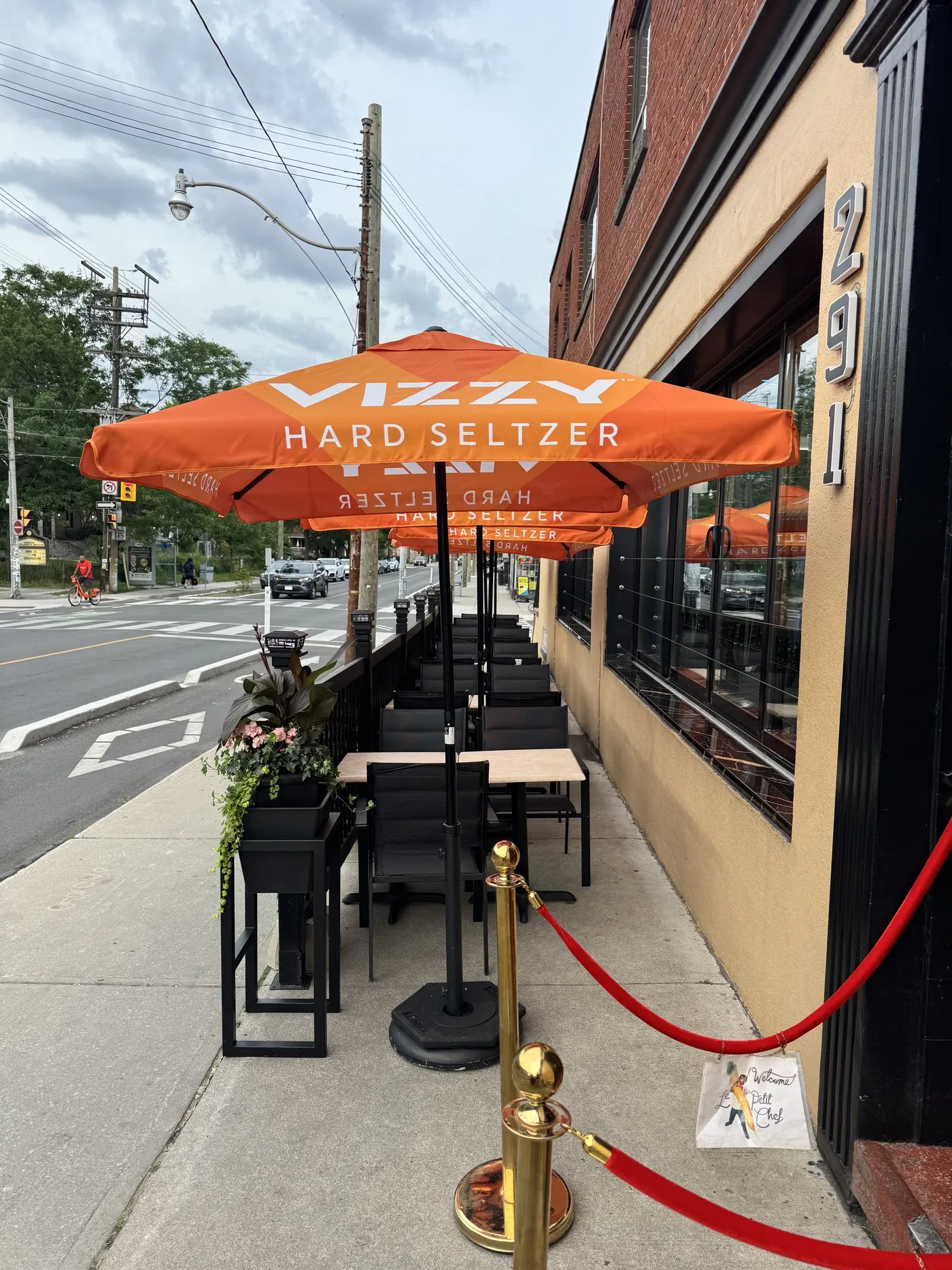 An open patio umbrella over bistro seating with a view up Harbord Street