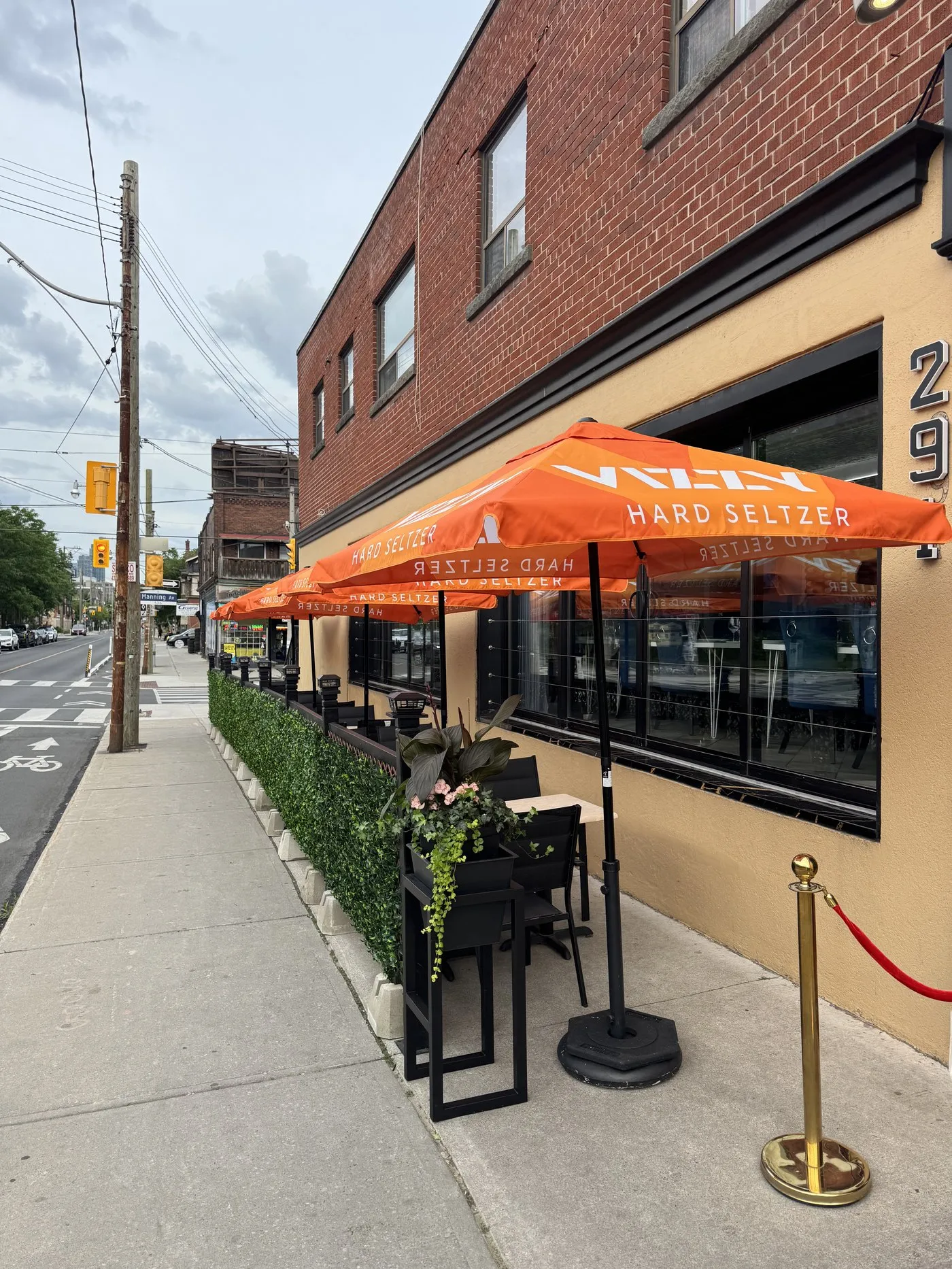 A planter of greenery beside shaded patio tables on the sidewalk